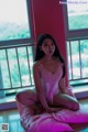 A woman sitting on a pink pillow in front of a window.