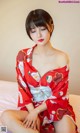 A woman in a red kimono sitting on a bed.